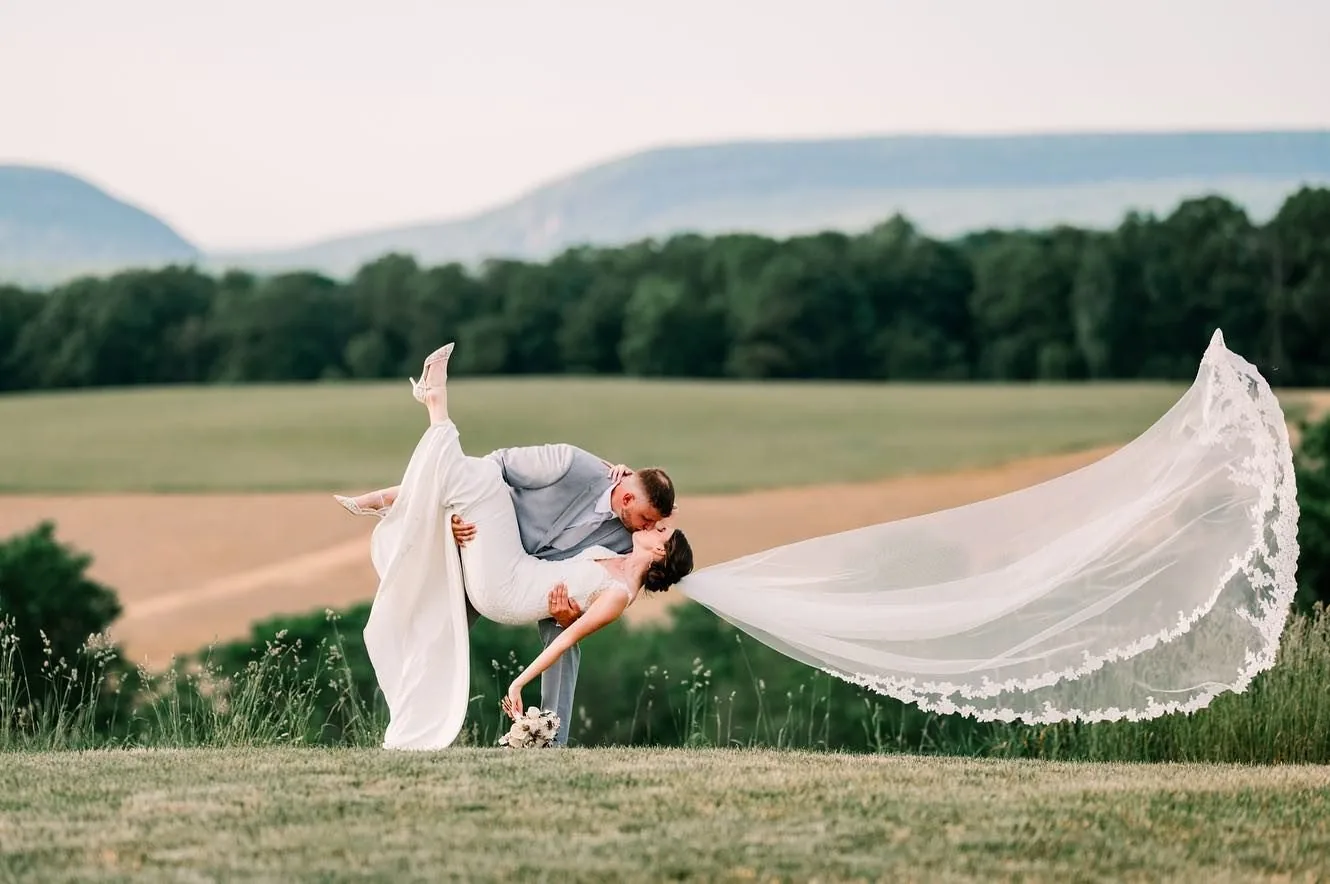 A groom dipping his bride on the hilltop, her veil flying above the valley and the Delaware Water Gap ridge