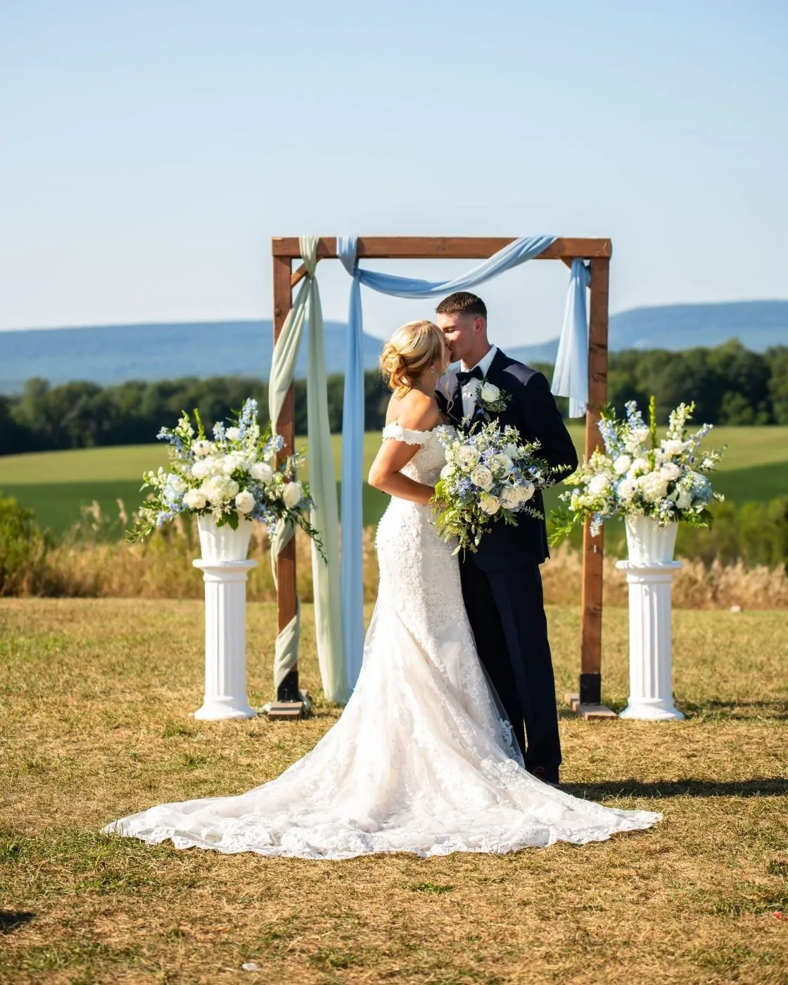 A couple at the ceremony arch with the mountains behind