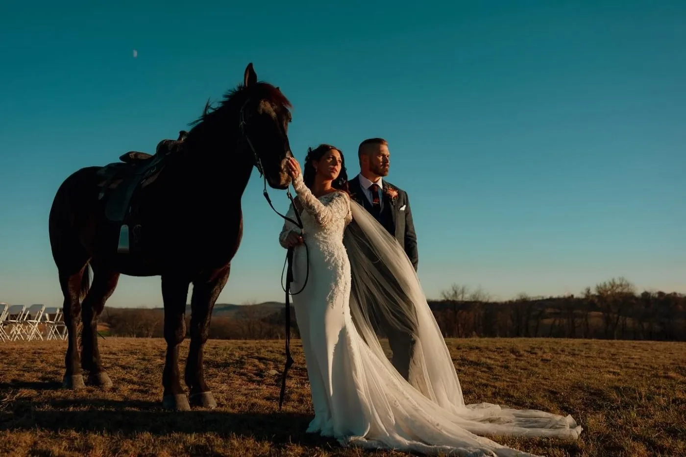 A couple at dusk beside a black horse in the pasture
