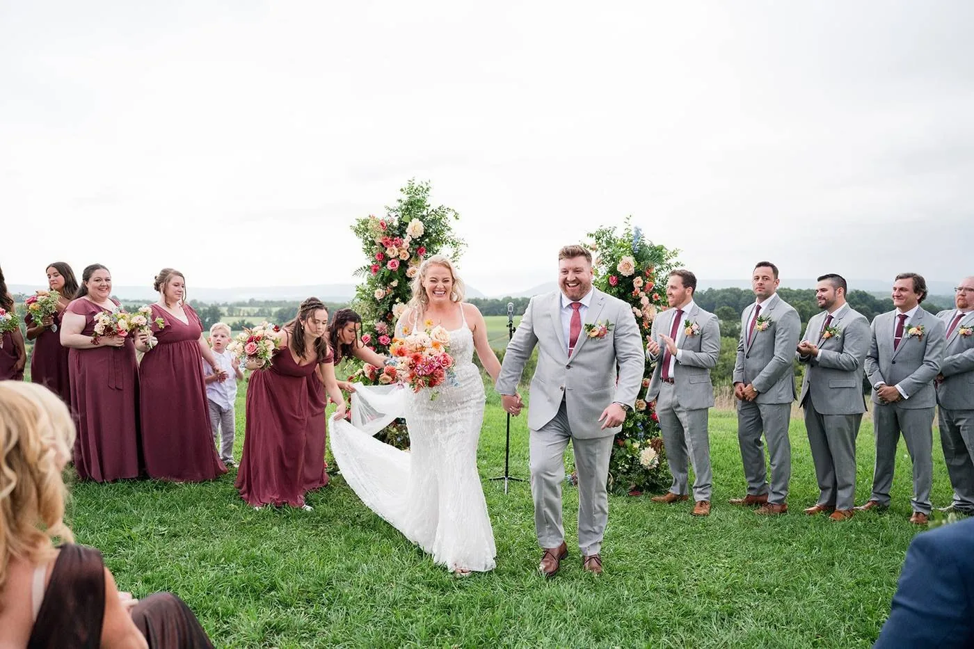 A couple walking back down the aisle past a floral arch on the mountaintop